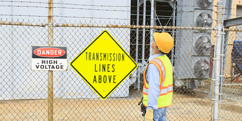 Worker Standing outsid ethe fence of a high voltage equiment yard looking at the warning signs on the fence