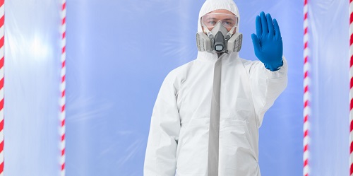 Photo of man in half-face respirator surrounded by caution tape holding up hand signaling viewer not to come any closer.